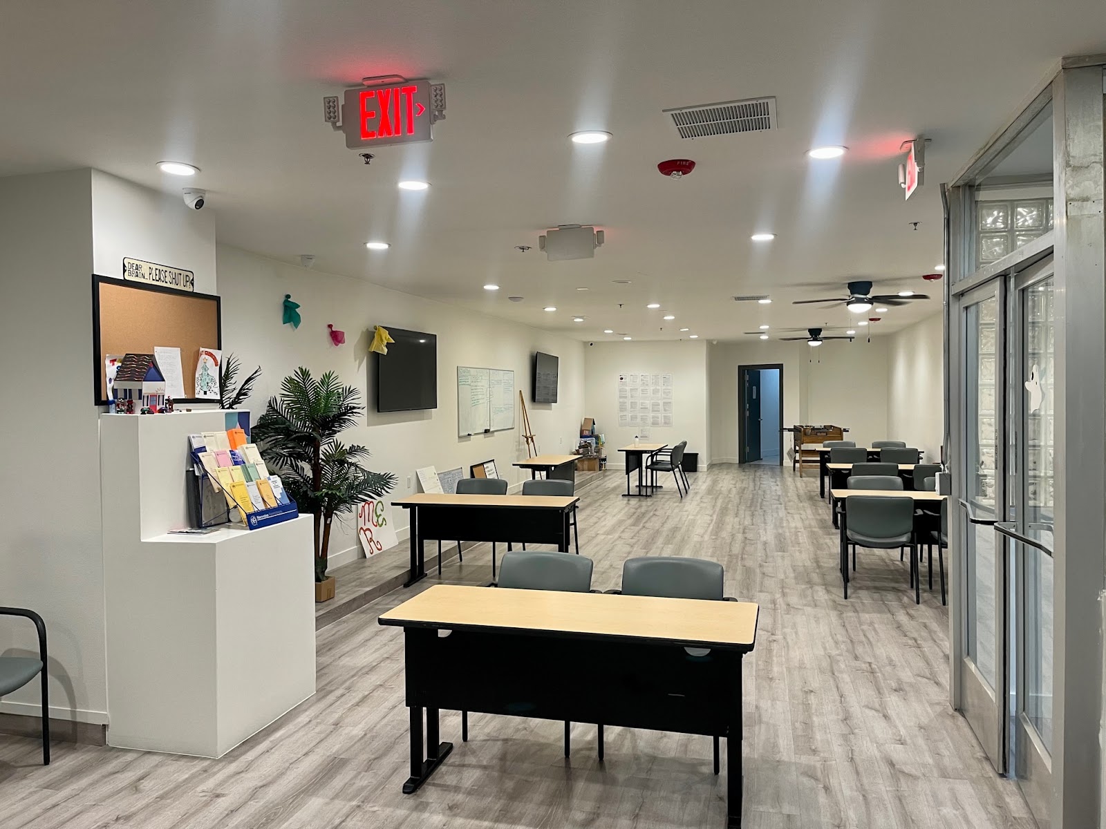 Interior common space with multiple desks, chairs, potted plants, informational displays and glass entries