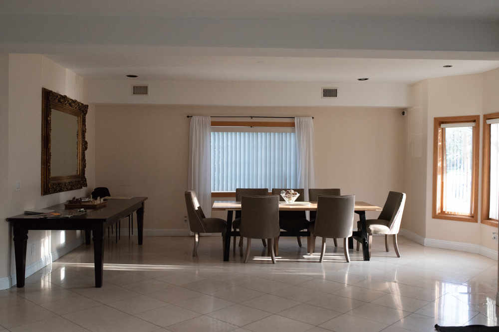 Interior common room with dining table and chairs, desk area, windows with curtains, and light tile flooring