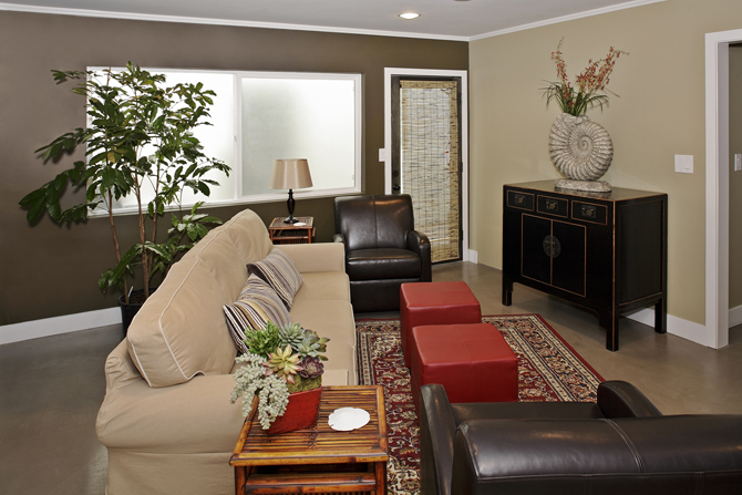 Interior living room with beige sofa, black leather seating, wood furniture, plants, and artwork