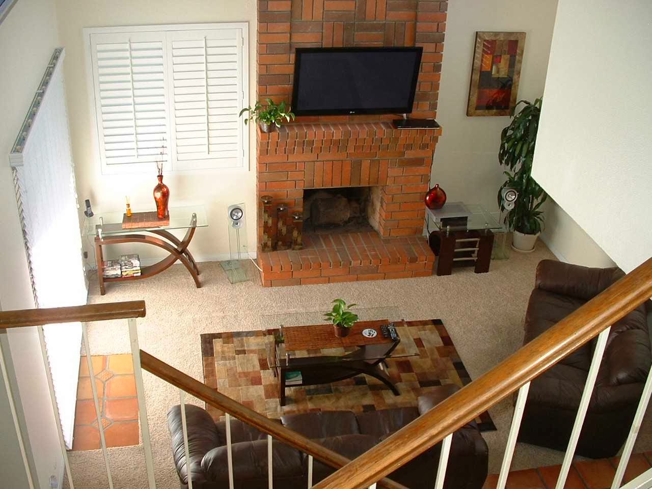 Interior living room featuring exposed brick fireplace with mounted television, wood staircase, seating area, and plants