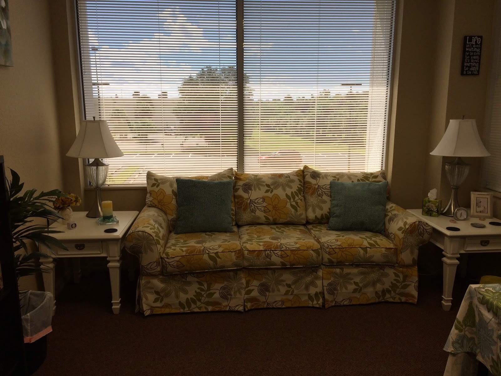 Interior lounge area with upholstered sofa, side tables, floor lamps, and natural window light