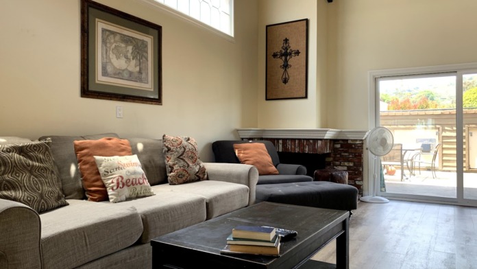 Interior common room with sectional sofa, framed artwork, and glass doors opening to ocean view terrace