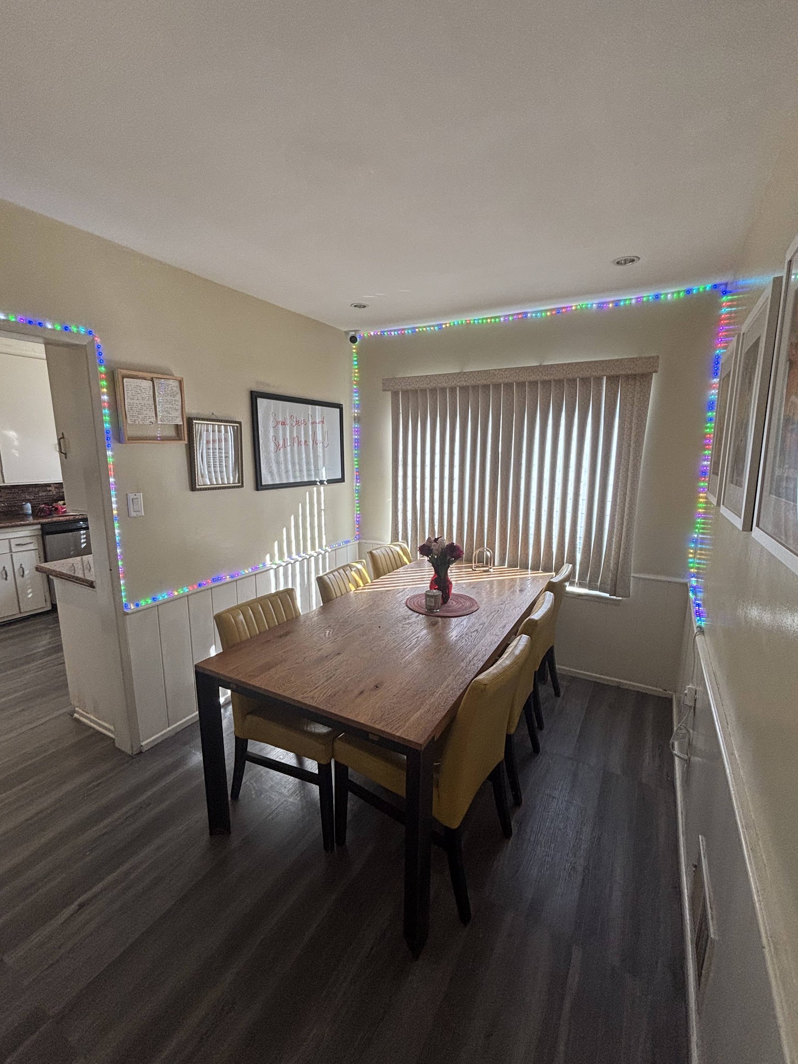 Interior dining room with wooden table, upholstered chairs, colorful LED strip lighting, and windows with blinds