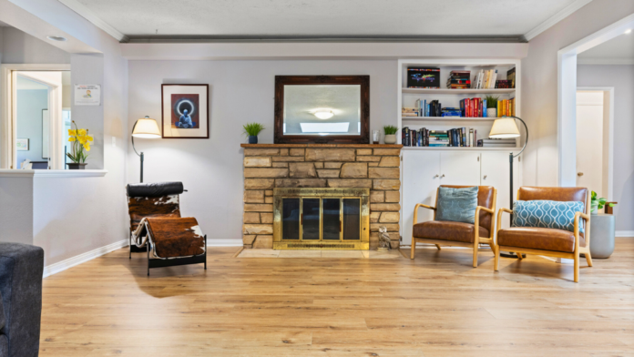 Interior community space with stone fireplace, comfortable seating, bookshelves, and hardwood flooring.