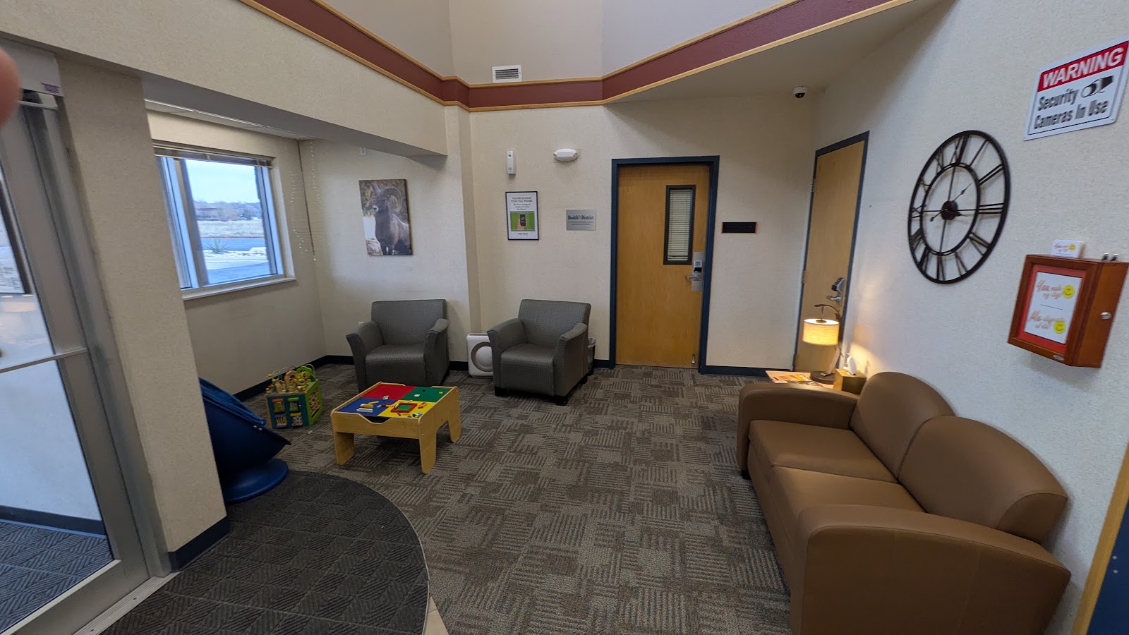 Interior common room with seating chairs, activity tables, wall clock, and floor-to-ceiling windows with mountain views