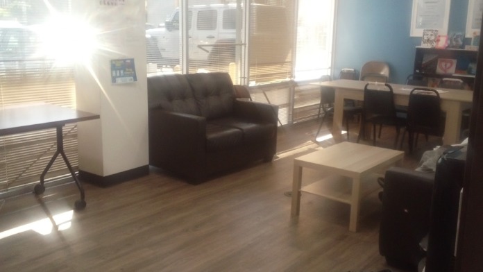 Interior lounge space with brown leather armchair, wooden coffee table, blue accent wall, and large windows with natural light
