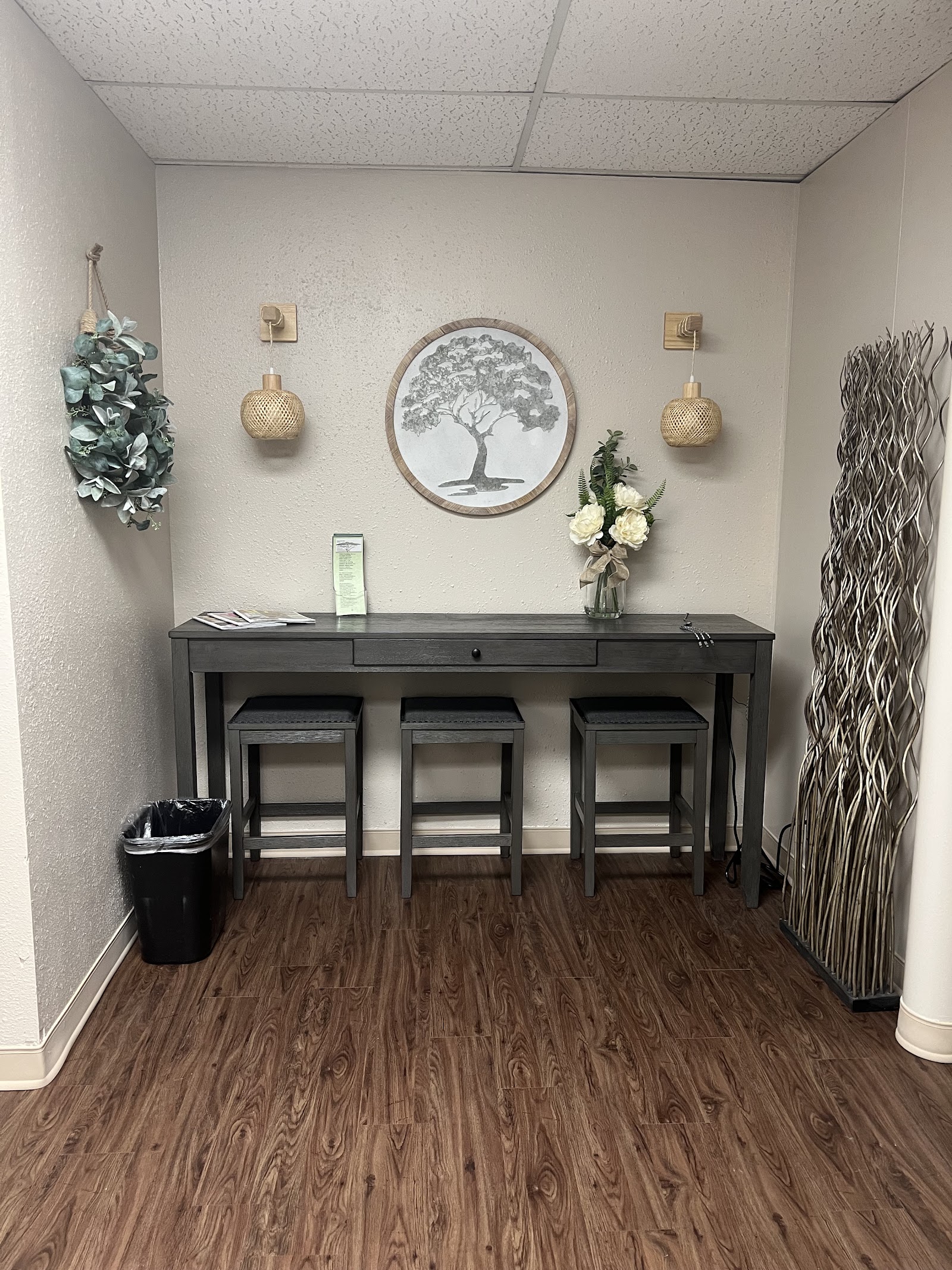 Interior counseling space with desk, stools, wall-mounted plant displays, and decorative tree artwork on walls