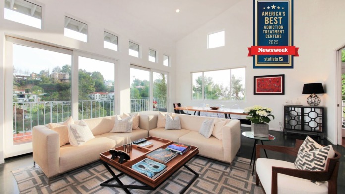 Interior living room with cream L-shaped sofa, large glass doors, modern furnishings, and decorative wall art overlooking landscaped grounds