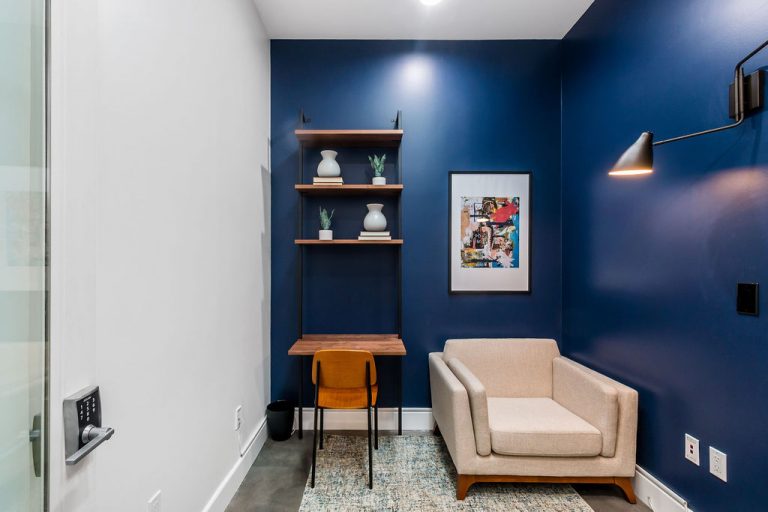 Interior counseling space with blue accent wall, armchair, desk with shelving, and contemporary lighting fixtures