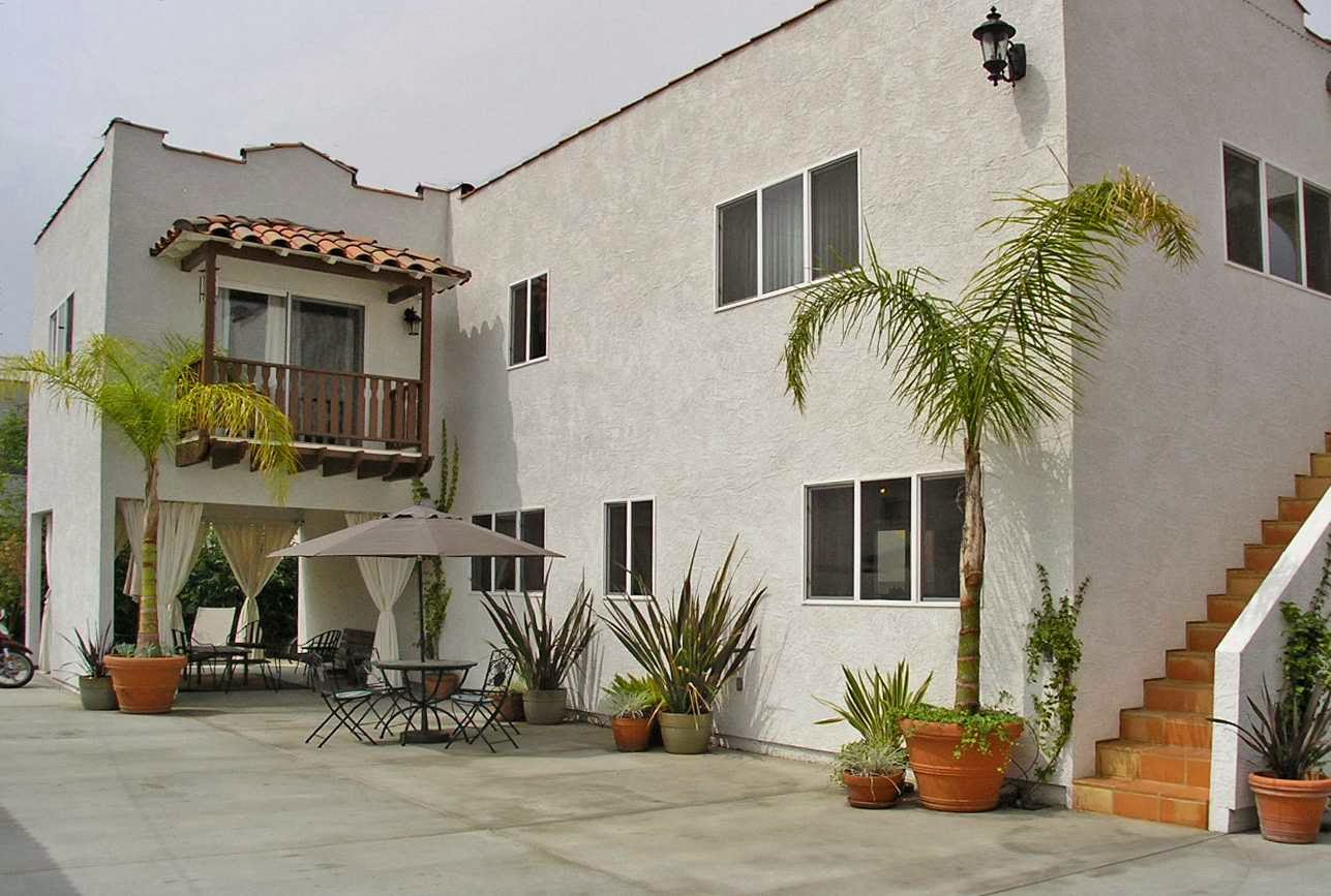 Exterior courtyard area showing stucco building, pergola, terra cotta tile flooring, potted plants, and seating space