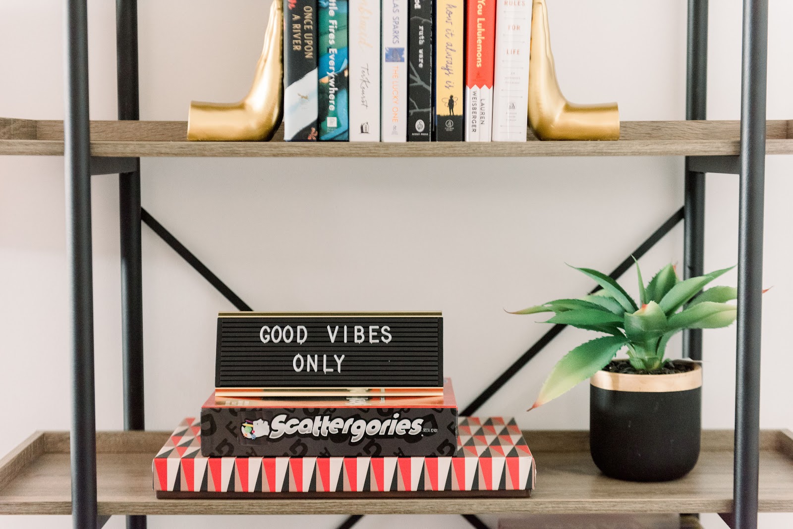 Interior close-up of decorative shelf displaying books, plants, and motivational letter board with 'Good Vibes Only' message