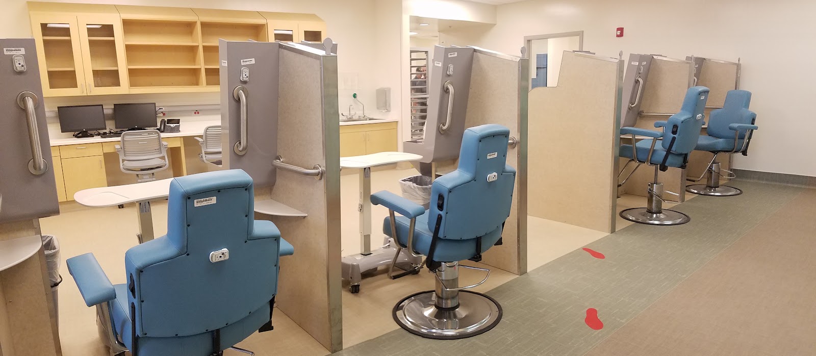 Interior dental clinic with multiple treatment chairs with blue upholstery, overhead dental equipment, and organized workspace with storage cabinetry