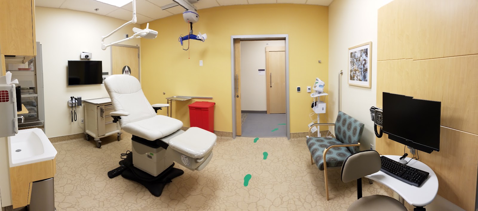 Interior dental treatment room with patient chair, overhead lighting, surgical equipment, and examination station with yellow accent walls