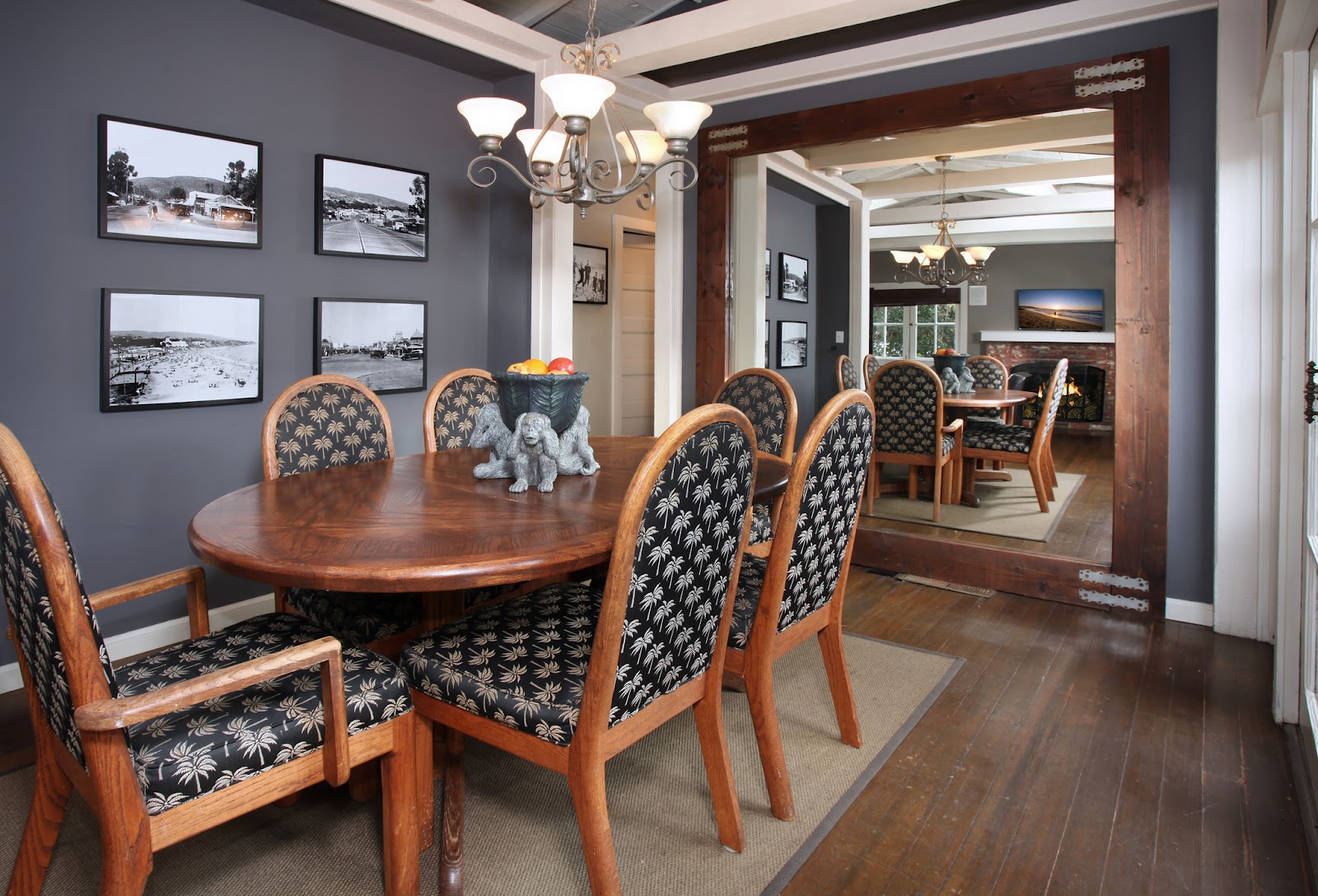 Interior dining room with oval wood table, upholstered chairs, chandelier, and framed landscape photographs