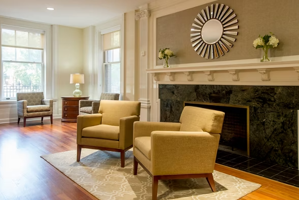 Interior living room featuring yellow accent chairs, fireplace with mantel, ornate mirror, large windows with natural light