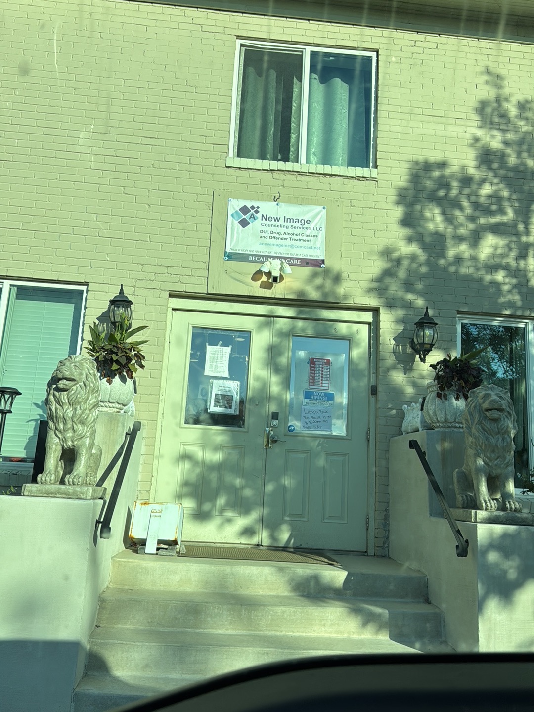 Entry vestibule with facility logo and business signage on green brick wall, lion planter statues, and glass entrance doors with steps