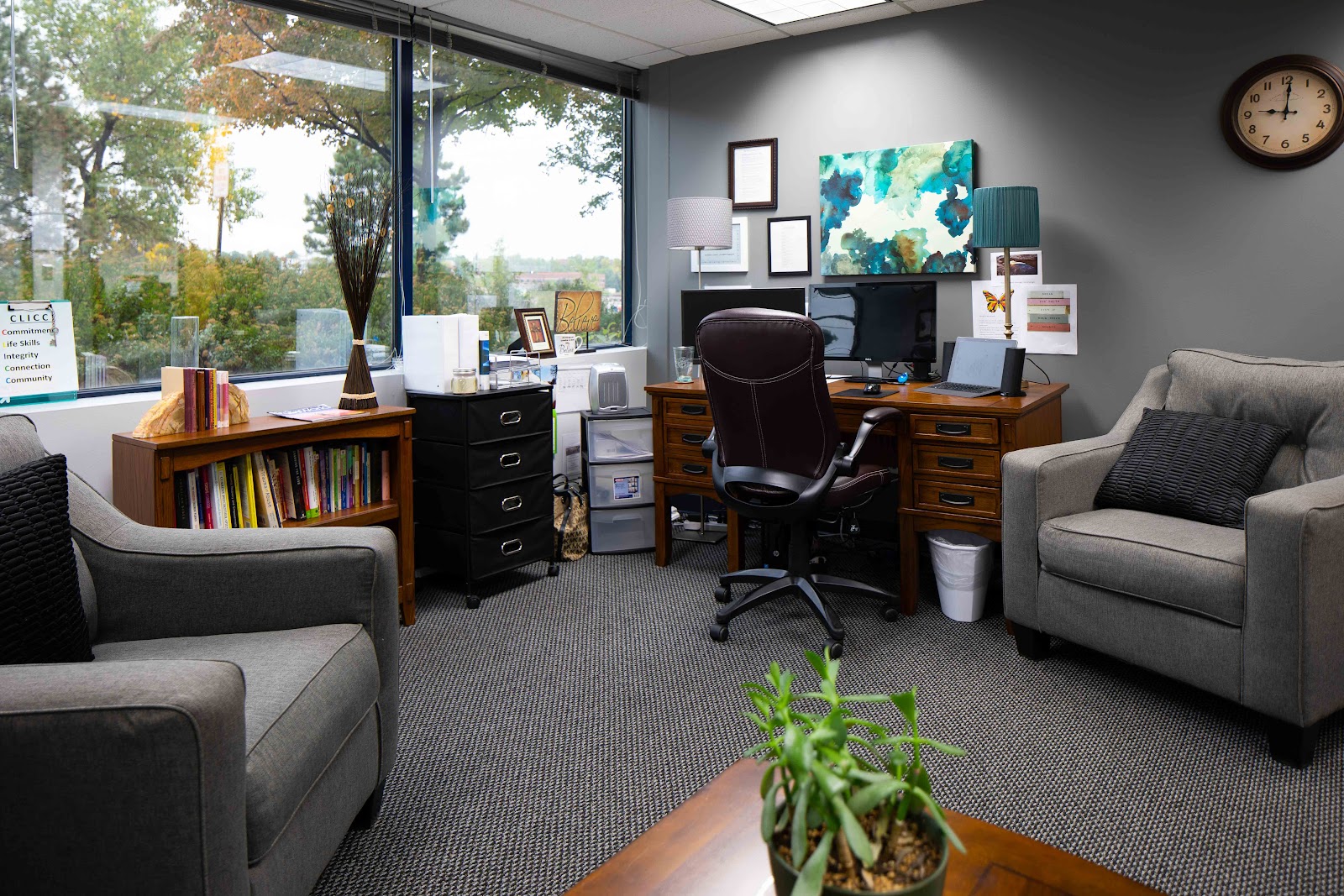 Interior office space with windows overlooking grounds, desk, seating, and natural lighting from expansive glass panels