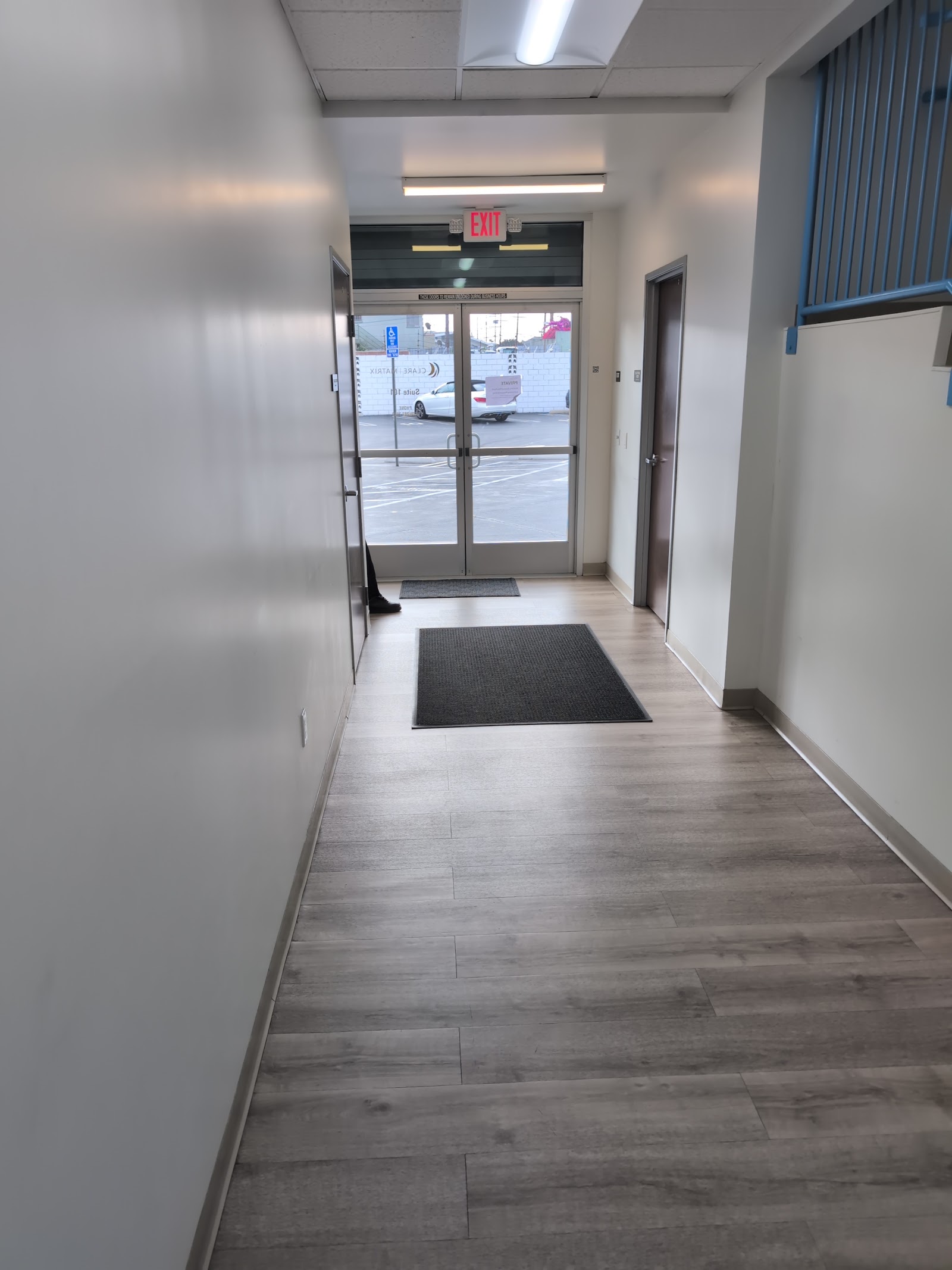 Interior hallway with wood flooring, exit sign, entrance doors with exterior view, and white walls