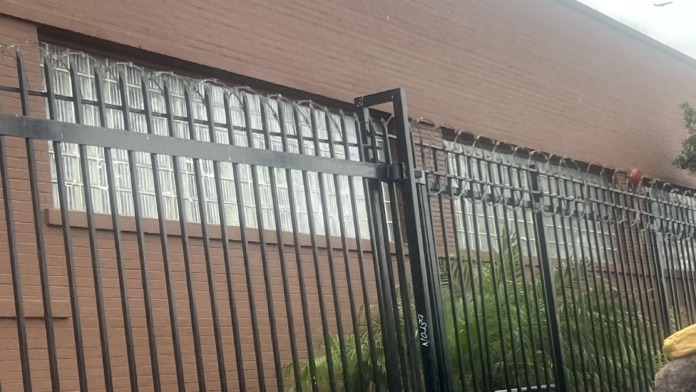 Exterior brick building facade with black metal security fencing and gate entrance