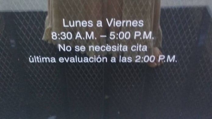 Exterior signage displaying weekday operating hours 8:30 A.M. to 5:00 P.M. and assessment procedures in English and Spanish