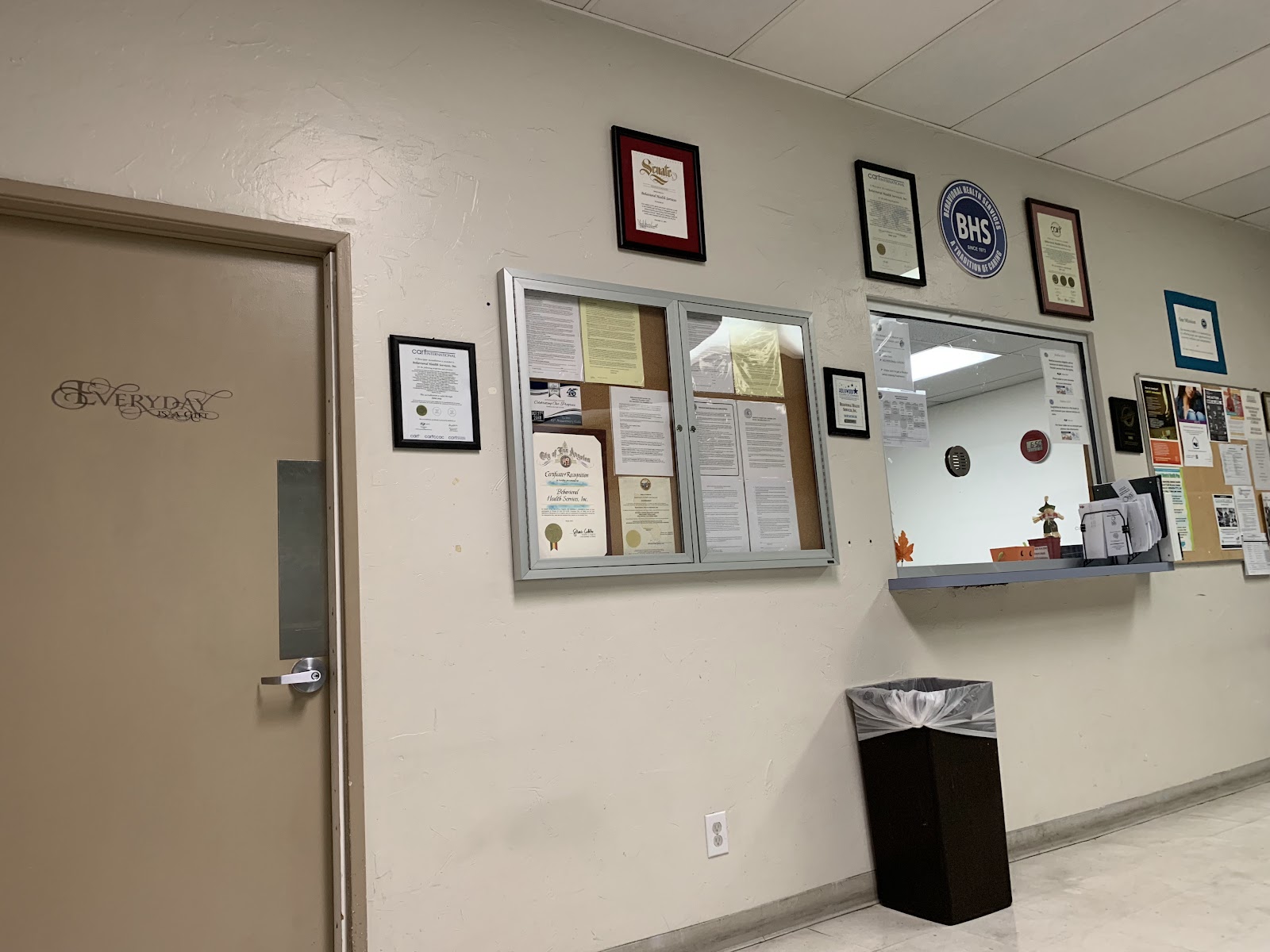 Interior hallway view with beige walls, framed certifications, reception area, and facility signage displaying credentials