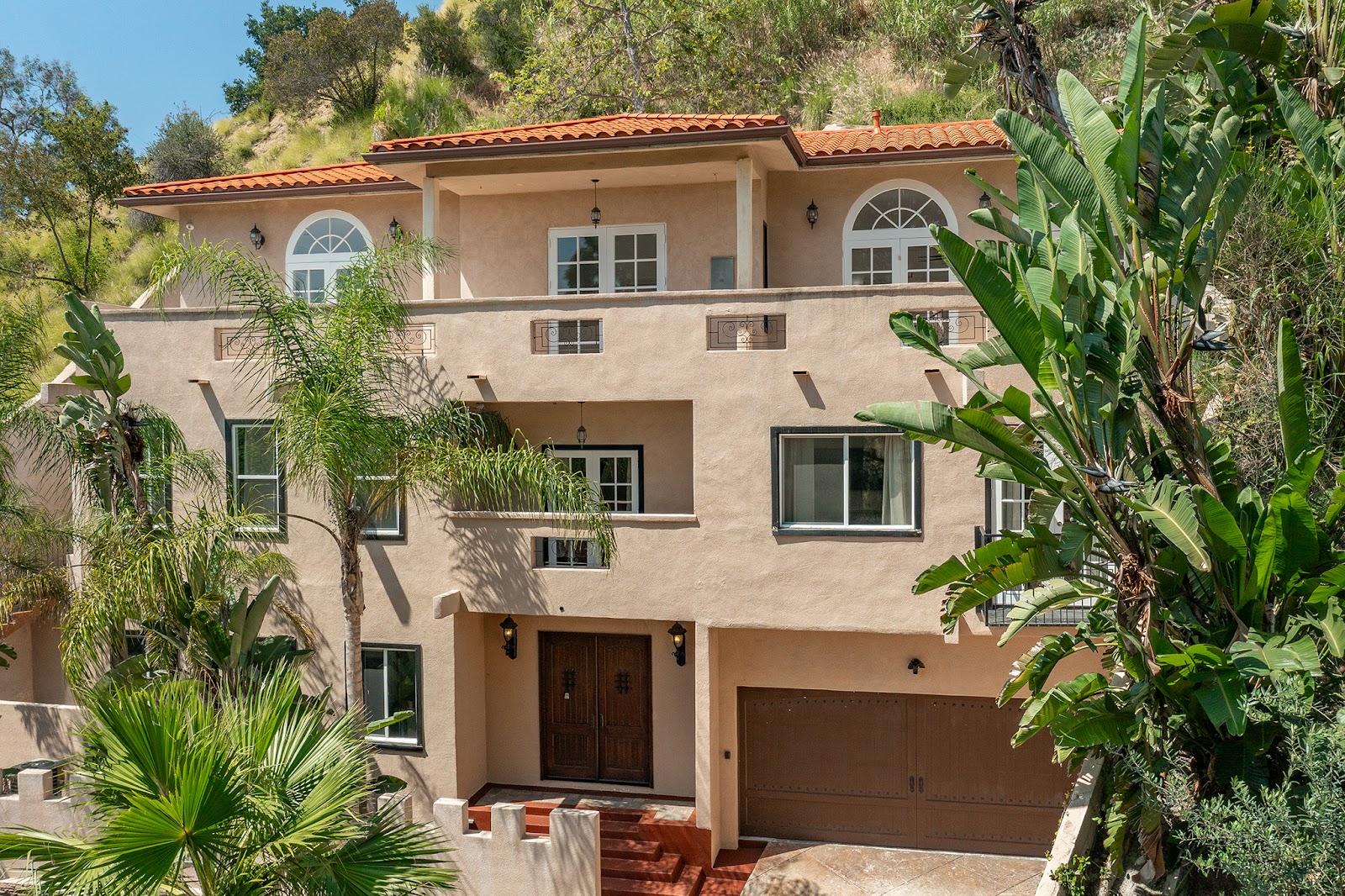 Exterior view of three-story residential treatment building with terra cotta tile roof, arches, balconies, and surrounding landscaping