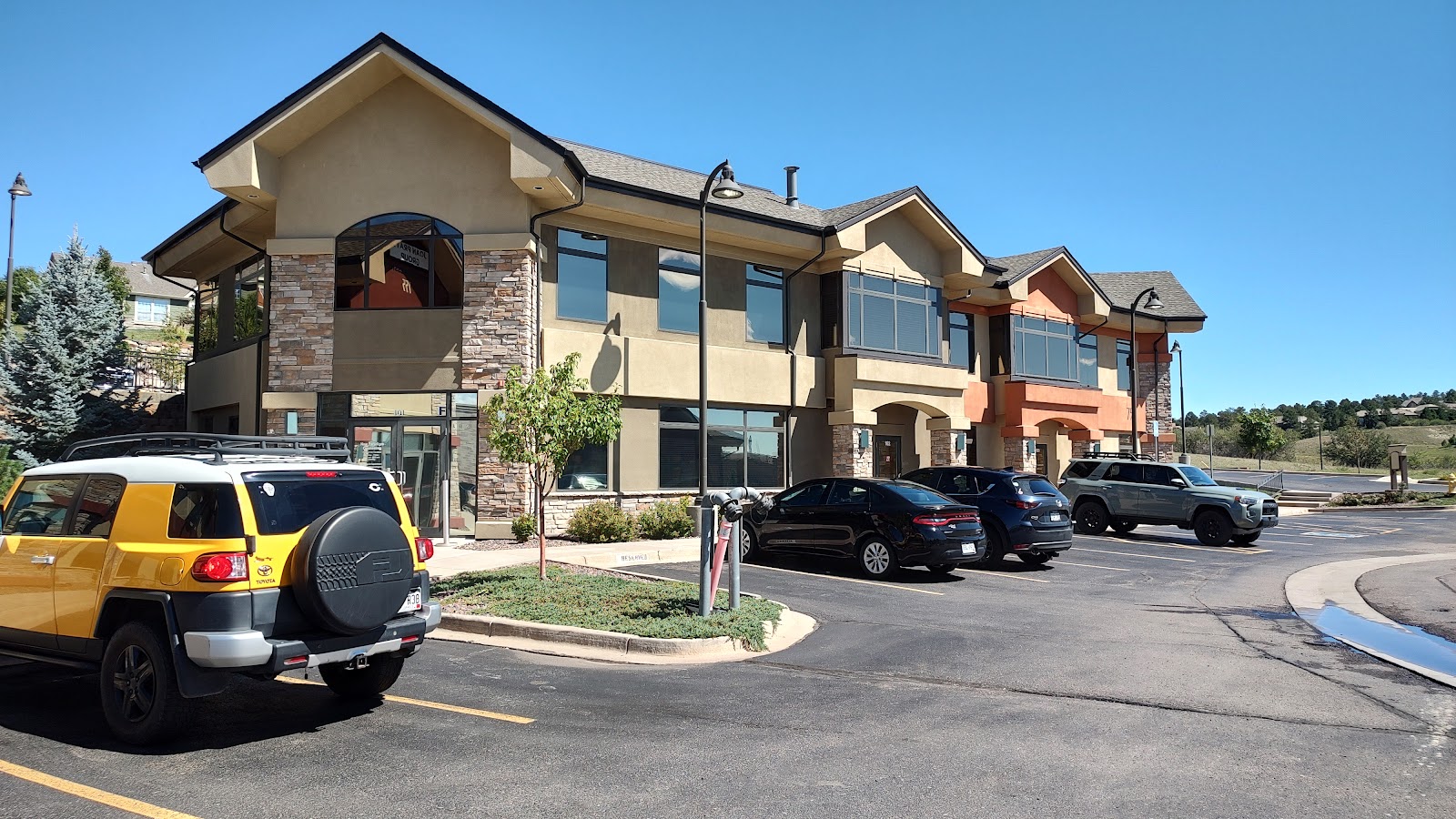 Exterior parking lot view showing multi-level facility building with stone and stucco construction, landscaping, and parked vehicles