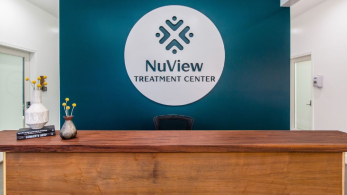 Interior reception desk with teal accent wall featuring NuView Treatment Center logo, wood desk, and decorative elements
