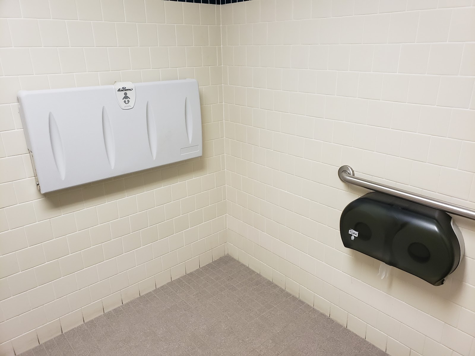 Interior restroom with tile walls, sink with hand soap dispenser, paper towel dispenser, and mirror