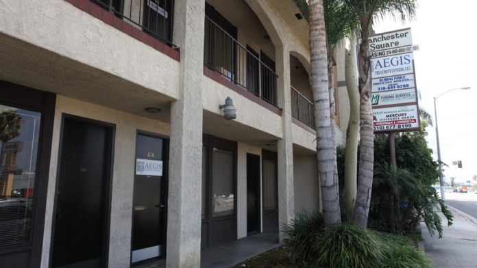 Exterior view of treatment center storefront with black glass doors, windows, and directory sign visible on stucco building facade
