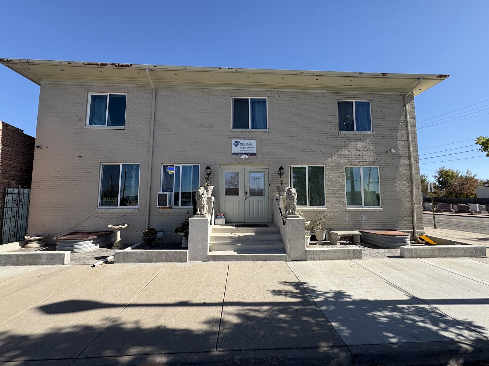 Exterior showing two-story cream brick building with flat roof, multiple windows, centered entrance with lion planters, and facility signage
