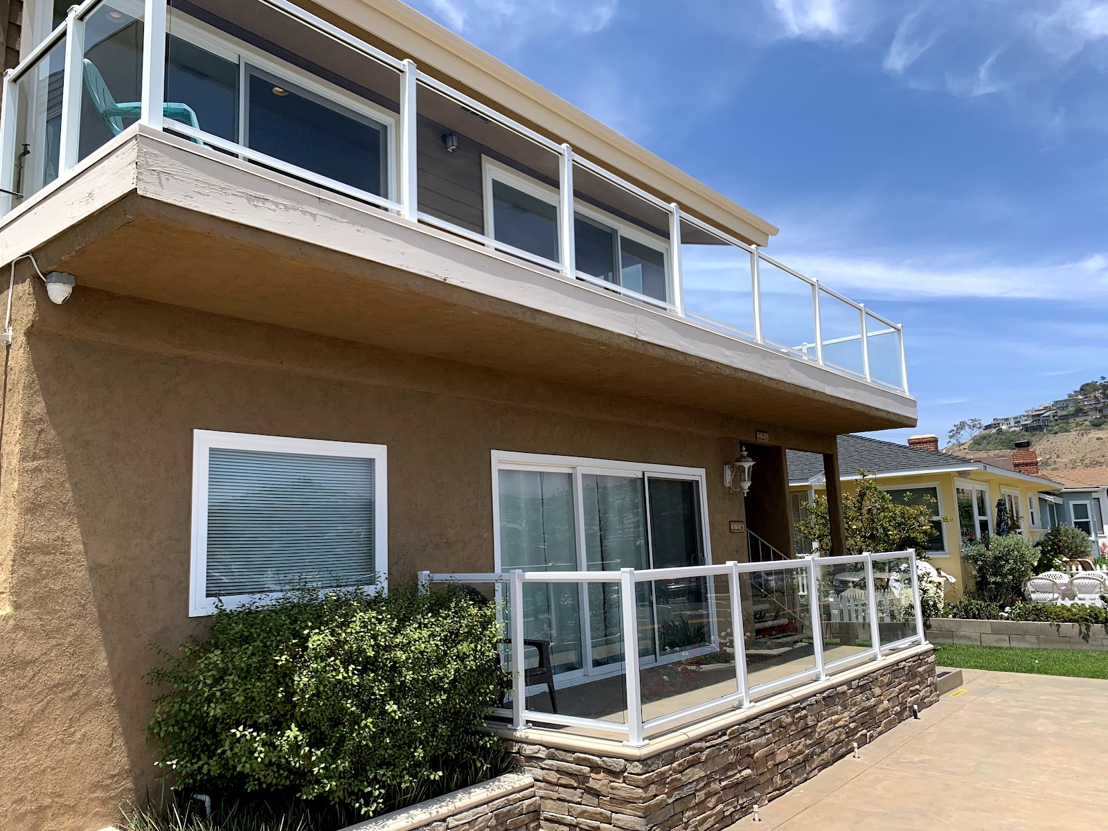 Exterior residential building showing tan stucco walls, white railings, windows, and landscaping
