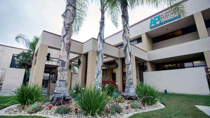Multi-story institutional building exterior with modern architecture, palm tree landscaping, decorative grounds, and facility logo on upper facade