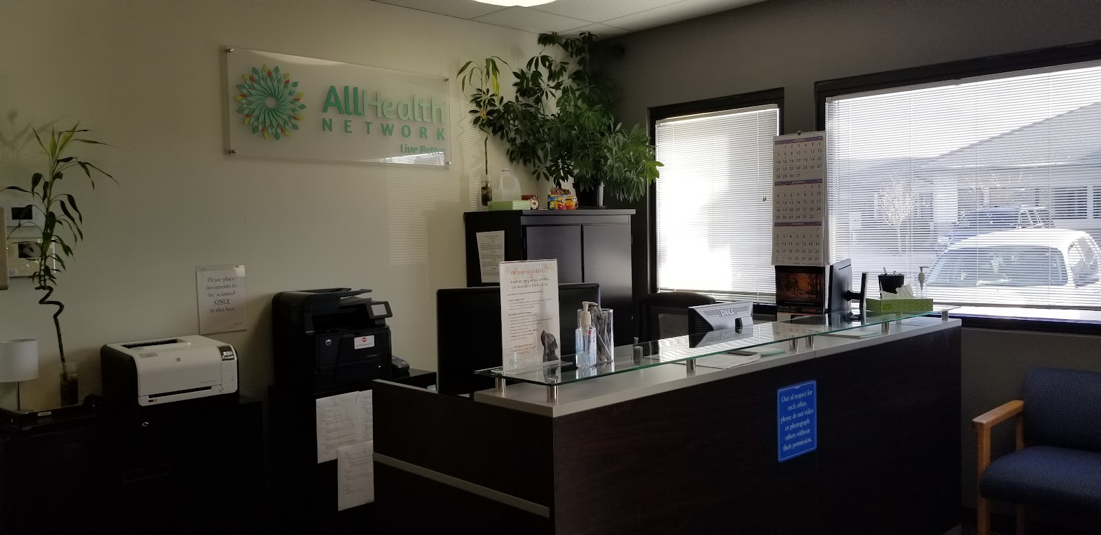 Interior reception counter with stone accents, AllHealth Network signage, and office equipment