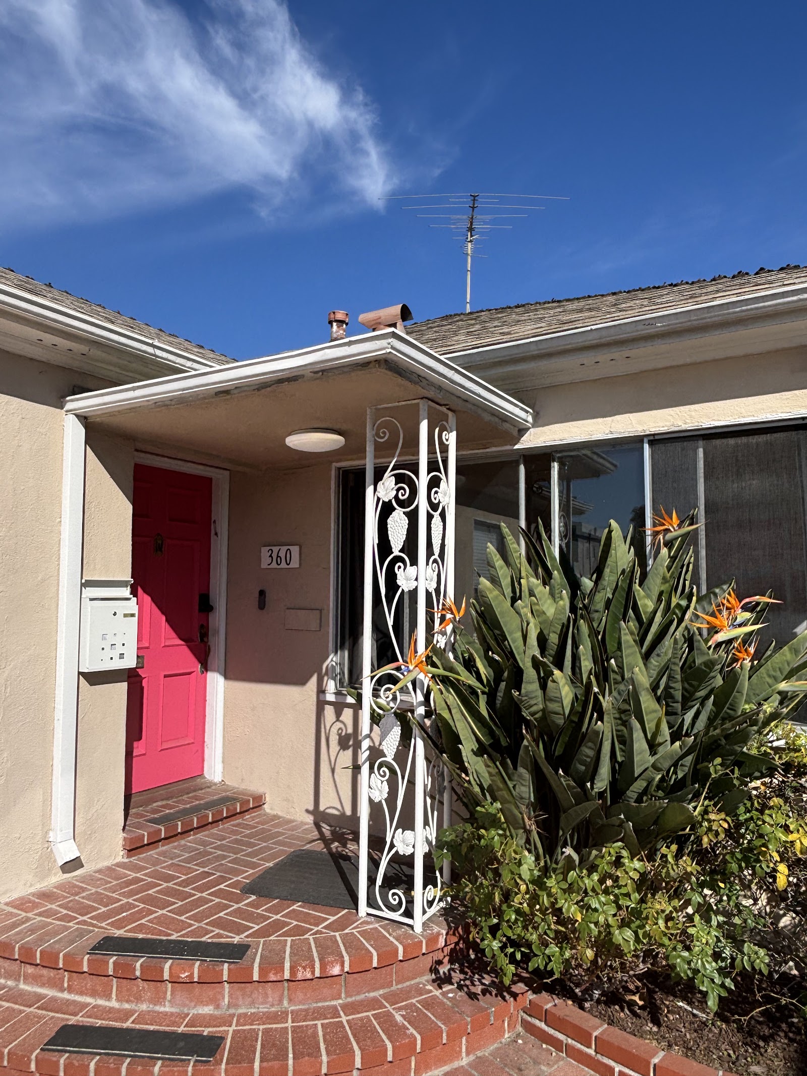 Exterior entrance showing red door with address number 360, decorative gate, and landscaping with cactus