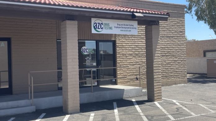 Exterior front entrance showing AZC Drug Testing signage, brick facade, metal door, and hours posted on window