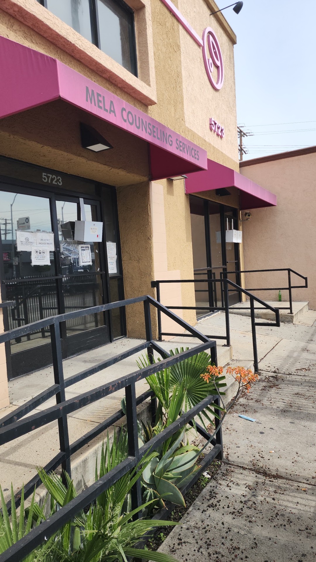 Exterior front entrance with black metal ramp rails, landscaping, and accessible entry to Mela Counseling Services facility