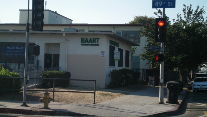 Exterior showing BAART facility white building with green signage at street corner intersection with traffic signal