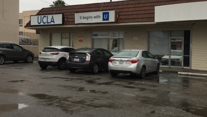 Exterior clinic building with UCLA signage, brown roof fascia, and parked vehicles in lot