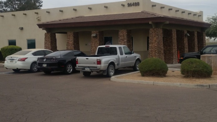 Exterior view of single-story treatment facility with tan stucco walls, brick columns, covered entrance, and parking area with vehicles