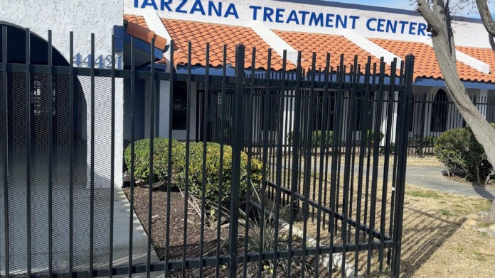 Exterior front view showing Tarzana Treatment Centers signage on white and terracotta building with black fencing and landscaped grounds