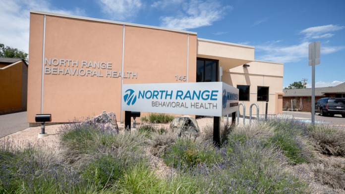 Exterior view of single-story behavioral health facility with North Range Behavioral Health signage, peach-colored facade, and native landscaping