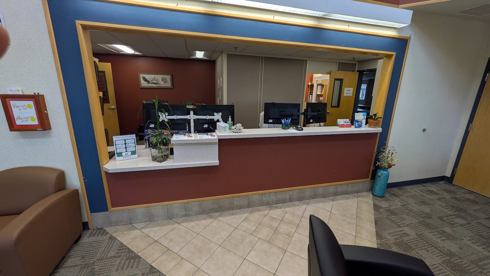 Interior reception area with burgundy and blue accent walls, white front desk counter, plants, and information display shelving