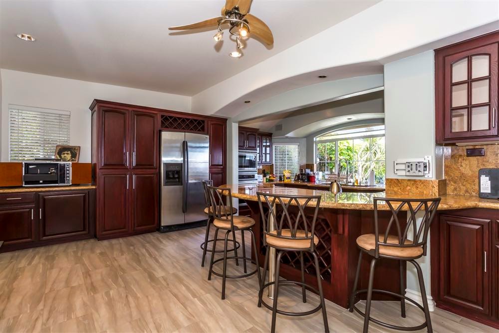 Large open kitchen with dark cabinetry, granite counters, stainless appliances, and bar seating for dining