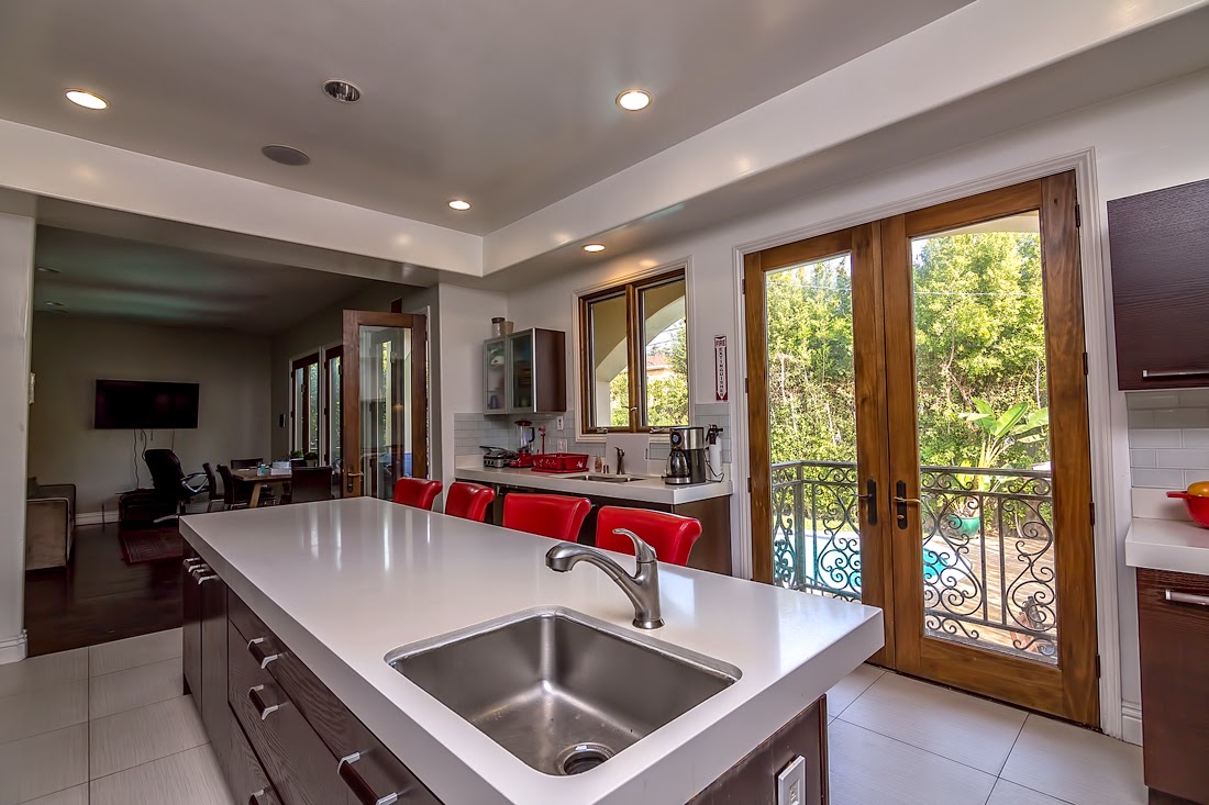 Interior kitchen and dining space with large island counter, stainless steel sink, wood cabinetry, red bar seating, and patio doors