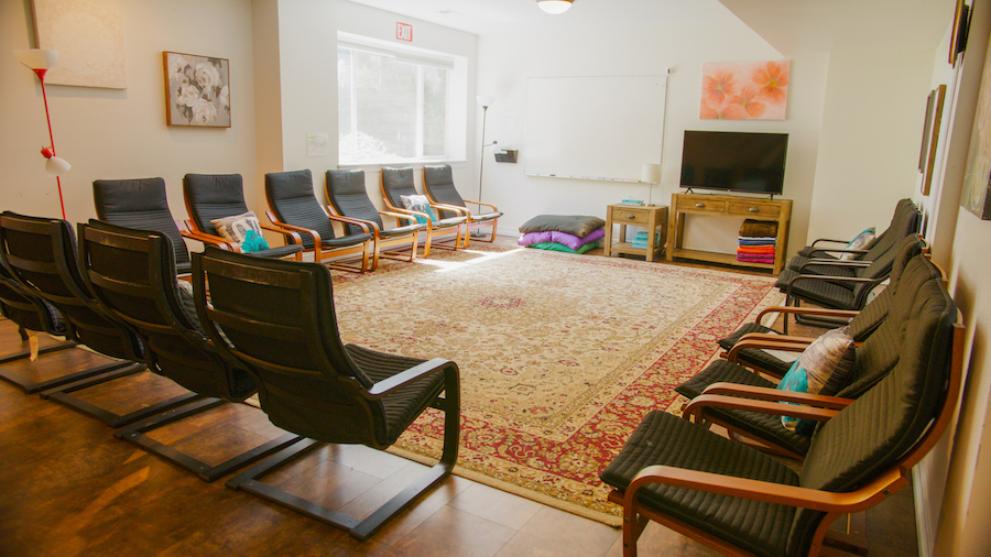 Interior gathering space with multiple black modern chairs arranged in rows, decorative cushions, television, and area rug.