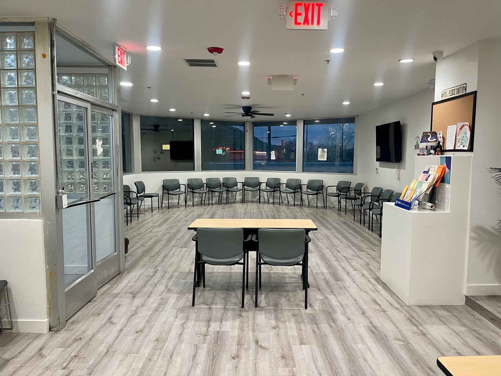 Interior meeting room with arranged seating, exit signage, large windows, wood flooring and facility materials