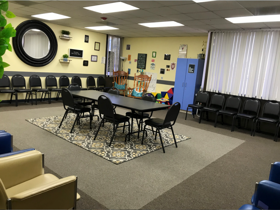Interior recreation space with yellow walls, multiple black chairs arranged around tables, and casual seating areas with decorative elements
