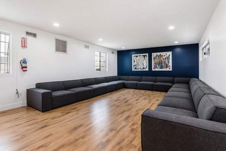 Interior lounge space with large black sectional sofa, blue accent wall, artwork, and modern furnishings for group sessions
