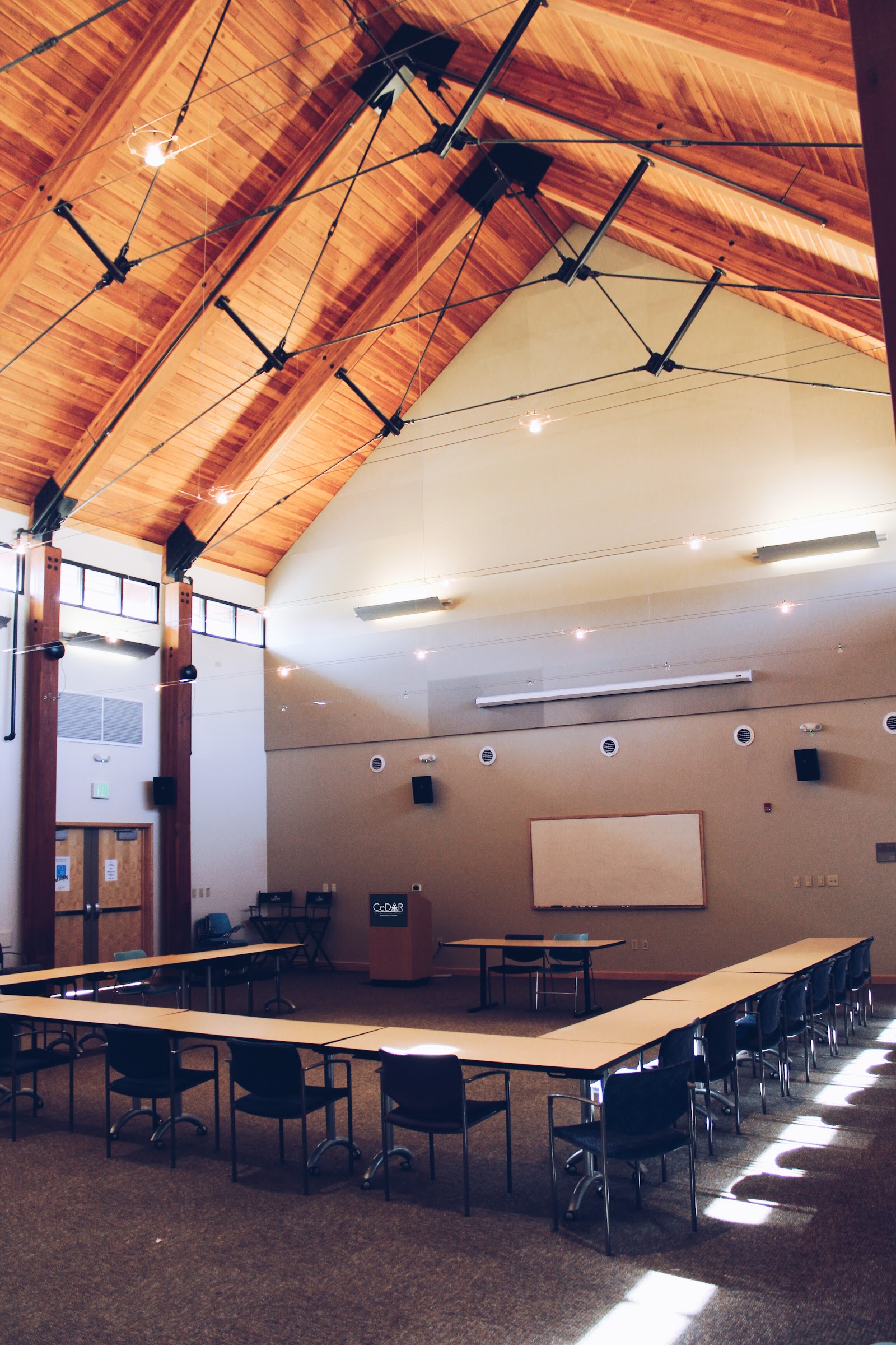 Interior large meeting space with wooden trusses, exposed beams, windows, tables and chairs for group gatherings.